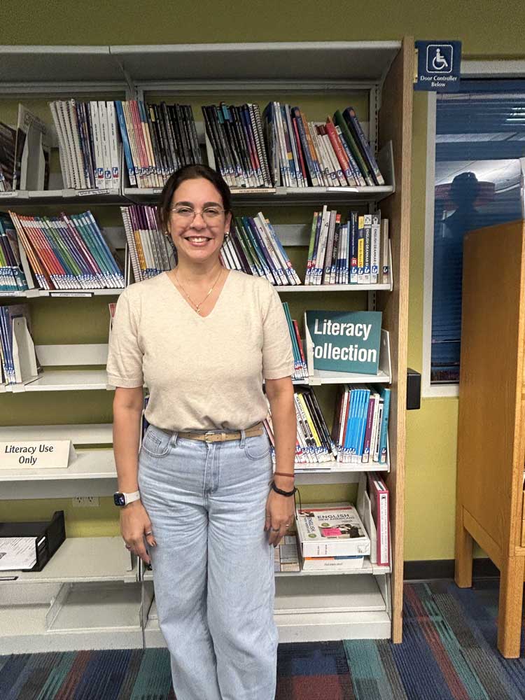 Maria standing in front of the Literacy Books on shelves at the library
